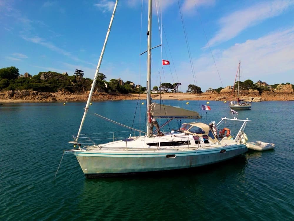 Segelyacht mit Schweizer Flagge vor Anker in einer Bucht mit rosa Granitfelsen und klarem, grünem Wasser