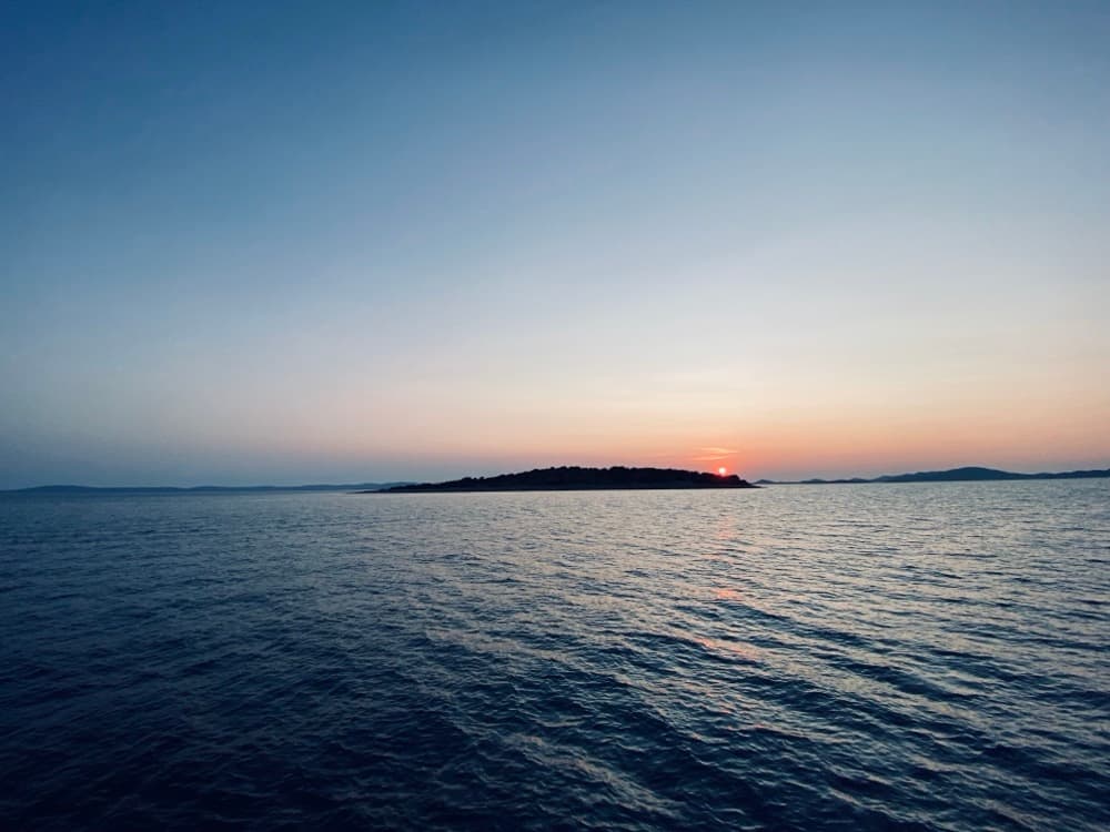 Sonnenuntergang über ruhiger See, am Horizont die Silhouette einer Insel