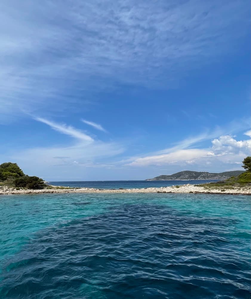 Türkisfarbenes Wasser in einer Bucht zwischen zwei flachen Inseln unter blauem Himmel