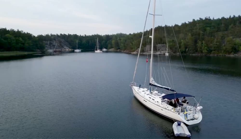 Segelyacht mit Beiboot vor Anker in einer stillen, bewaldeten Bucht mit Felsufern